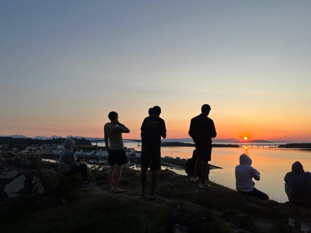 Backpackers stand watching the sunset from a hill on the Isle of Skye, meet new people, discovering Scotland, unique travel experience, Scotland's hidden gems